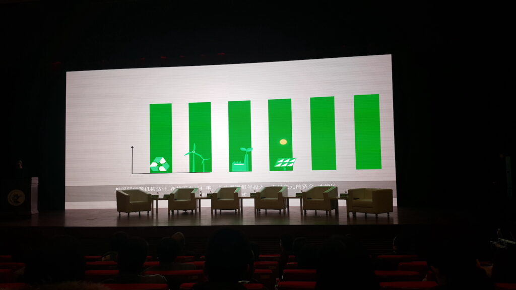 Photo of stage with empty chairs and vertical green bars on the screen behind.