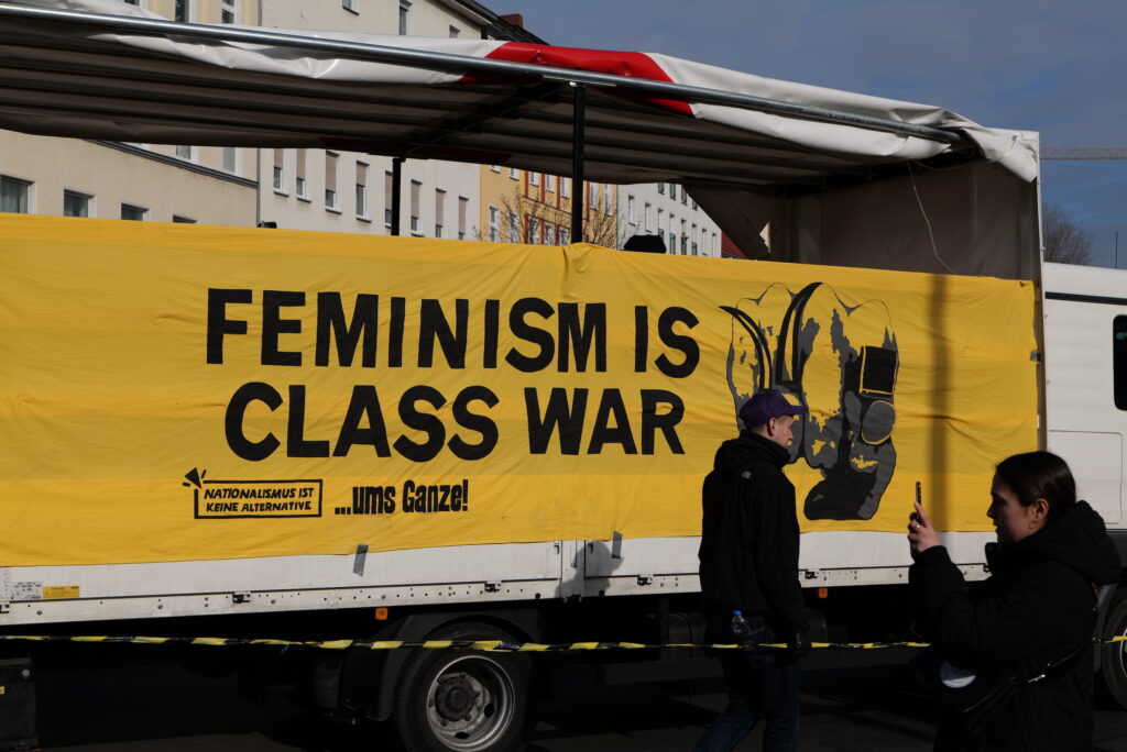 A yellow banner hanging on the side of a trailer reads Feminism is Class War.